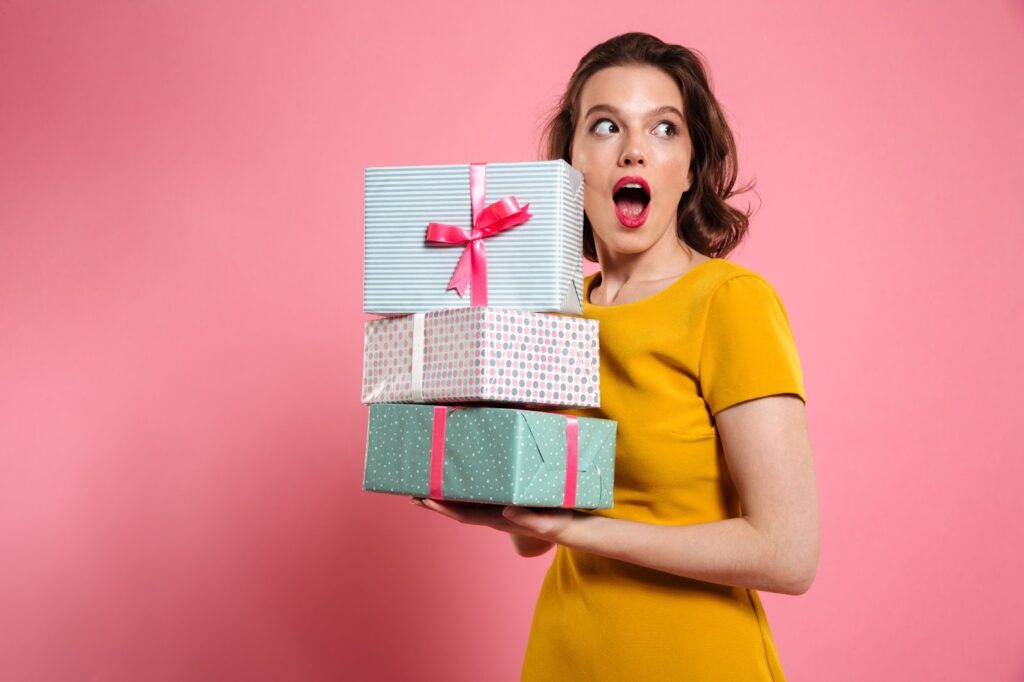 Shocked girl with bright makeup holding heap of presents