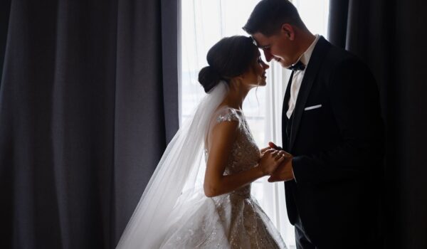 Groom and bride standing face to face in room holding hands