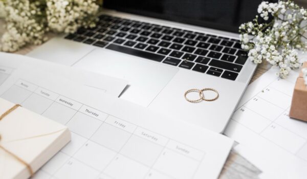 Close-up of calendar, wedding rings and laptop on desk
